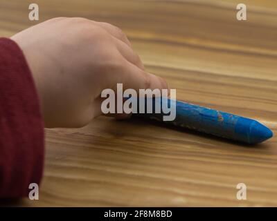 primo piano della mano di un bambino che tiene un pastello, su uno sfondo di legno chiaro Foto Stock