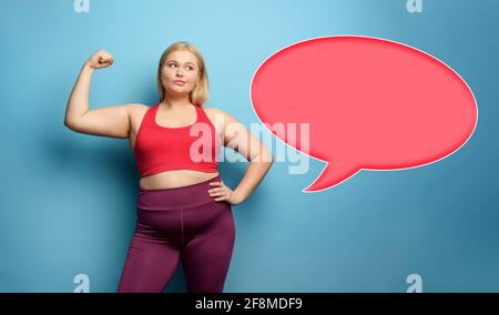 Fat girl fa la palestra a casa. Espressione premurosa. Sfondo ciano Foto Stock