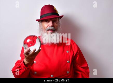 Uomo americano in pensione con una camicia rossa e fedora cappello che esamina con attenzione una palla di cristallo Foto Stock