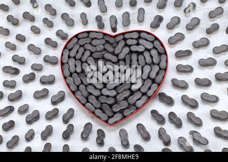 Cardbox a forma di cuore con noccioline nere impaccate granulato protettivo in plastica frizzante Styrofoam chip di fondo. Concetto di giorno di amore o di San Valentino Foto Stock