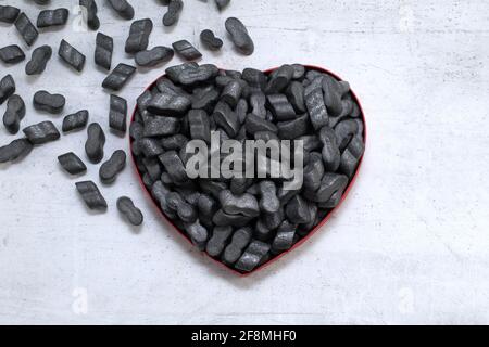 Cardbox a forma di cuore con noccioline nere impaccate granulato protettivo in plastica frizzante Styrofoam chip di fondo. Concetto di giorno di amore o di San Valentino Foto Stock