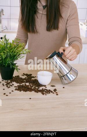 Donna in una cucina scandinava leggera versa il caffè da un macchina da caffè in tazza al mattino Foto Stock