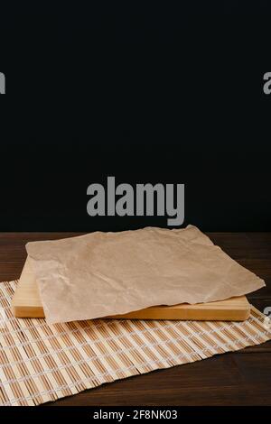 Tagliere e un foglio di carta sgualcita su un il tappetino si trova su un tavolo di legno marrone su un nero sfondo Foto Stock