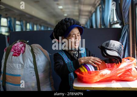 (210415) -- XICHANG, 15 aprile 2021 (Xinhua) -- UNA donna del gruppo etnico Yi organizza i suoi beni acquistati dalla città di Xichang sul treno 5634 nella provincia sudoccidentale del Sichuan, 12 aprile 2021. Mentre i moderni treni ad alta velocità passano davanti a nuove stazioni in tutta la Cina, un paio di treni a bassa velocità attraversano ancora le montagne Daliang. I 5633/5634 treni collegano Puxiong e Panzhihua della provincia di Sichuan con una velocità media inferiore a 40 km all'ora. Il viaggio con 26 stazioni in mezzo dura undici ore e quattro minuti, con i prezzi dei biglietti che variano da 2 yuan a 25.5 yuan (circa 0.3-3. Foto Stock