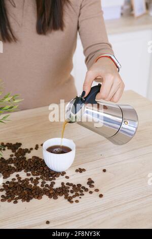 Donna in una cucina scandinava leggera versa il caffè da un macchina da caffè in tazza al mattino Foto Stock