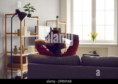 Vista posteriore di felice rilassata giovane donna nera seduta su comodo divano a casa Foto Stock