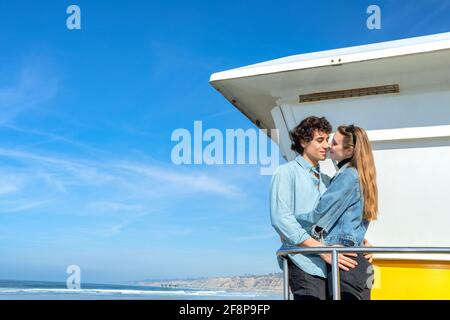 Una giovane coppia intrecciata di fronte ad una torre di bagnino Foto Stock