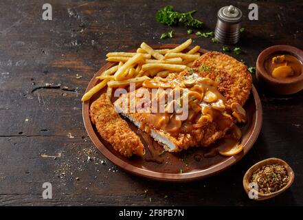 Un angolo alto di deliziosa scaloppina di carne impanata guarnita con delizioso salsa cremosa di champignon condita con patate fritte Foto Stock