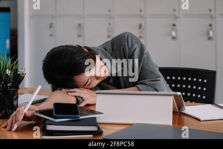 Donna d'affari stanca overworked che dorme sul tavolo in ufficio. Giovane ragazza esausta che lavora da casa. Donna che usa un computer portatile. Imprenditore, affari Foto Stock