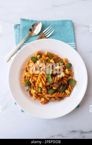 Fusilli di grano integrale Pasta Arrabbiata con verdure. Pasta di verdure con zucchine, funghi, mais e peperoni su un piatto bianco. Foto Stock