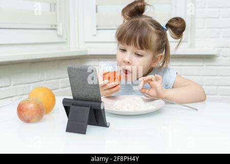 ragazzina che mangia cibo e guarda i cartoni animati su uno smartphone Foto Stock