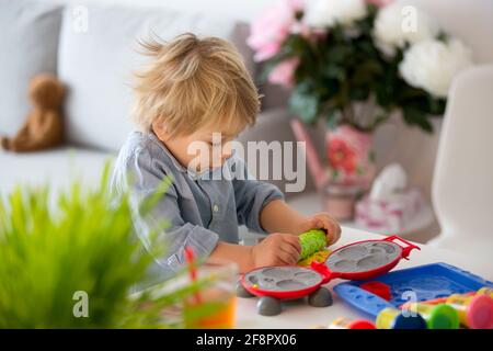 Carino bambino biondo, dolce ragazzo, giocando con il gioco DOH modelline a casa, facendo diversi oggetti Foto Stock