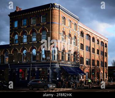 Londonuk - 14 Aprile 2021: Serata di London Street scena di open pub (vecchio pub), ciclisti, pedoni, ciclisti con sole basso Foto Stock