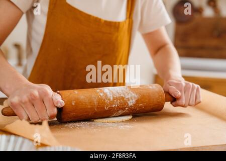 Mani di pasticciere che arrotolano l'impasto con la coppiglia sul tavolo Foto Stock