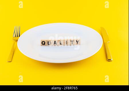 Primo piano di blocchi di legno con parola DI QUALITÀ su un bianco piastra con un coltello e una forcella Foto Stock