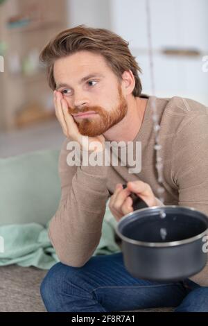 uomo che tiene il secchio e che raccoglie l'acqua dal soffitto Foto Stock