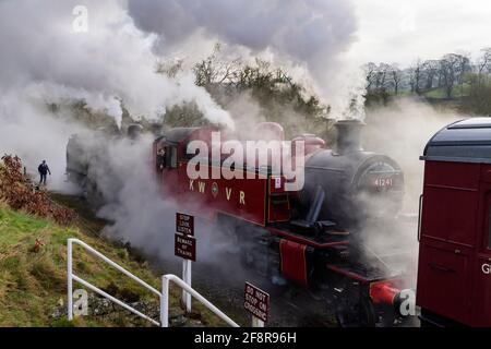 Treni storici a vapore (locos) che soffia drammatiche nuvole di fumo si fermò all'attraversamento (conducente di motore in cabina) - ferrovia storica, KWVR, Yorkshire Inghilterra UK. Foto Stock