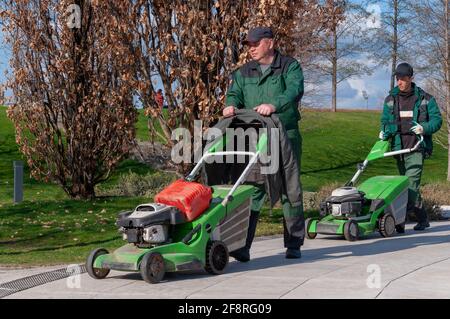 Krasnodar, Russia - Aprile 14 2021: Due tosaerba in uniforme camminano attraverso il parco in tempo soleggiato per tagliare l'erba Foto Stock