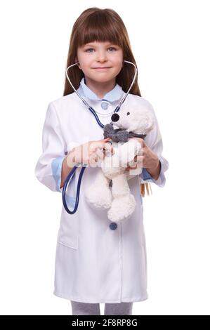 Dottore ragazza in camice medico bianco ascolta i battiti cardiaci con stetoscopio su orso giocattolo su sfondo bianco isolato Foto Stock