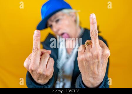 Divertente ritratto di donna matura. Lady mostra il dito medio vestito come un rapper arrabbiato. Donna matura su sfondi colorati Foto Stock