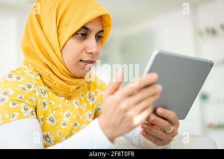 Donna musulmana che lavora su tablet a casa sua Foto Stock