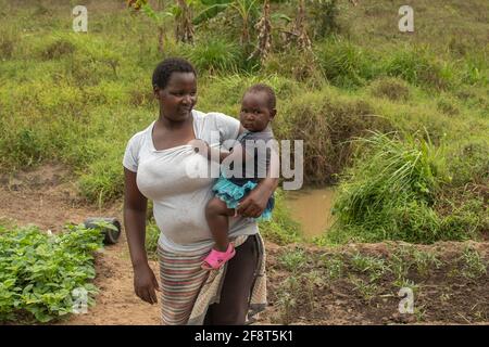 Dodoma, Tanzania. 08-18-2019. Una madre sta portando il suo bambino sulle sue braccia dopo una dura giornata di lavoro alle piantagioni di ortaggi campo. Foto Stock