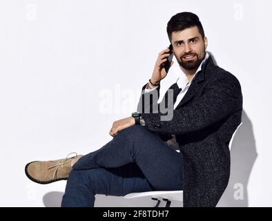 Un uomo sorridente in jeans e un'elegante giacca a tweed casual usa il suo smartphone. Vista laterale, testa ruotata Foto Stock