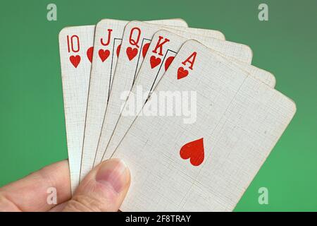 Germania. 09 aprile 2021. Carte da gioco di una mano di poker da un vecchio gioco di carte, mano francese, con un colore reale, il più alto flusso diritto nel poker, composto da dieci, jack, regina, re e asso di un colore, tenuto da una mano nel cancello contro uno sfondo verde. | utilizzo in tutto il mondo credito: dpa/Alamy Live News Foto Stock