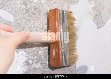 Il repairman wets vecchia carta da parati con acqua con un pennello - un metodo per rimuovere la vecchia carta da parati dalla parete Foto Stock