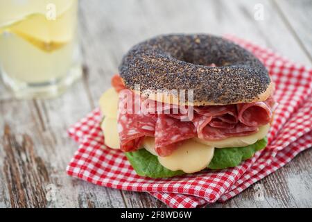 Bagel con salame, formaggio, pomodoro e insalata fresca. Foto Stock