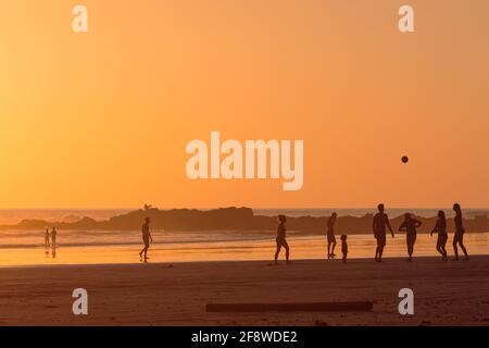 Famiglia e amici che giocano sulla spiaggia al tramonto Foto Stock