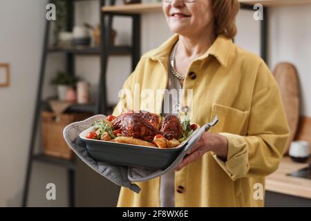 Primo piano di una donna anziana che serve pollo arrosto per il tavolo delle feste a casa Foto Stock