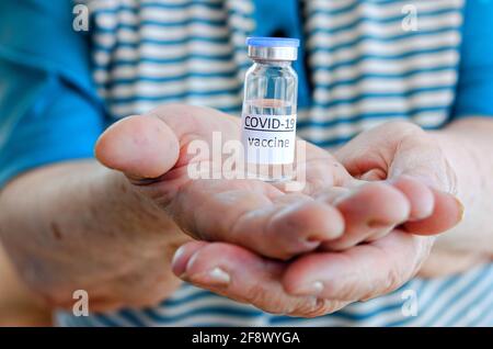 Donna anziana in T-shirt blu contenente flacone di vaccino flacone di vetro per la vaccinazione contro COVID-19 SARS-COV-2 coronavirus pandemico in mani. Foto Stock