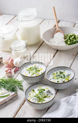 Tradizionale zuppa estiva fredda di yogurt fatto in casa, cetrioli ed erbe fresche su un tavolo di legno Foto Stock