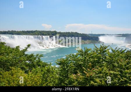 Vista tra gli alberi alle Cascate canadesi e americane del Niagara con barca turistica sull'acqua in tempo soleggiato Foto Stock