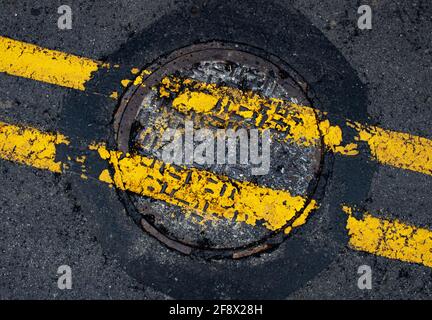 Copertura fognaria in ghisa arrugginita con Yellow Painted Road Linee divisorie nel mezzo di una Pennsylvania Street in Contea di Lancaster Foto Stock