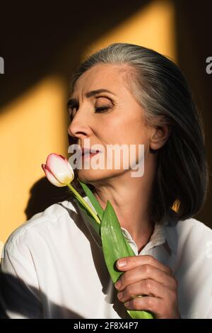 Donna matura in camicia bianca con tulipano su sfondo giallo con ombra Foto Stock
