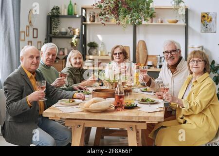 Ritratto di un gruppo di vecchi amici seduti al tavolo da pranzo con bicchieri di vino durante la cena Foto Stock