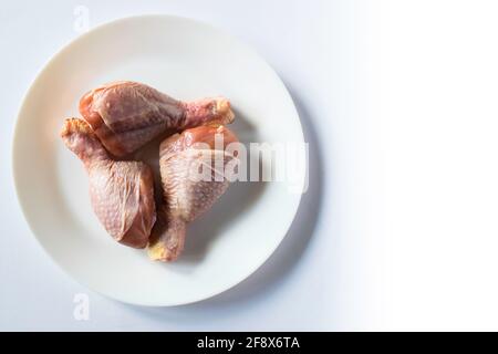 Cosce di pollo crude su piatto bianco con qualche extra negativo spazio sul lato destro Foto Stock