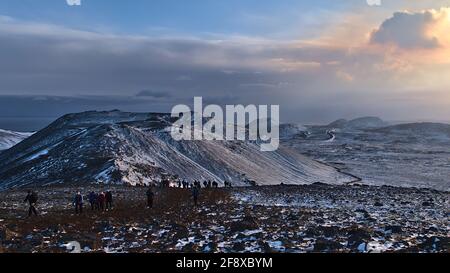 Le persone che camminano verso il vulcano recentemente eruttato a Fagradalsfjall nelle valli di Geldingadalir con splendida vista panoramica sulle montagne innevate. Foto Stock