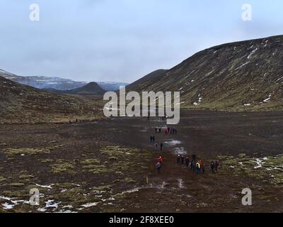 Persone che camminano verso il vulcano recentemente eruttato a Fagradalsfjall montagna in Geldingadalir valli con il paesaggio vulcanico ruvido in nuvoloso giorno d'inverno. Foto Stock