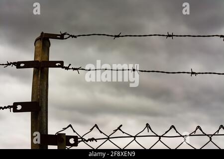 Due file di filo spinato sulla parte superiore di una recinzione con nubi tempesta sullo sfondo. Concetto di immigrazione, fuga o libertà Foto Stock