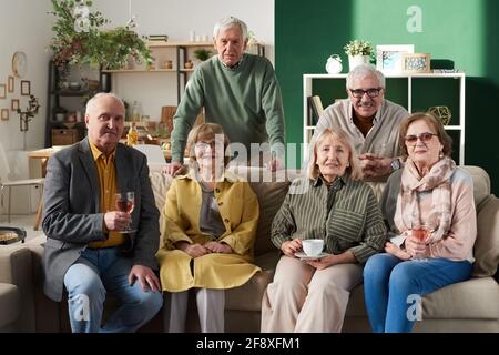 Ritratto di gruppo di vecchi amici seduti sul divano e. sorridendo alla macchina fotografica durante la riunione nella stanza Foto Stock