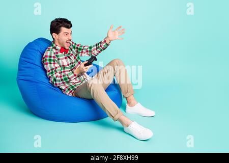 Foto profilo di arrabbiato uomo sit borsa tenere gamepad aperto bocca indossare plaid camicia cravatta pantaloni isolato colore blu sfondo Foto Stock