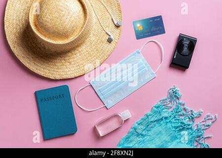 Cappello di paglia, passaporto, maschera medica, disinfettante per le mani, carta di credito e piccola macchina fotografica su sfondo rosa. Vacanze estive durante l'epidemia di coronavirus Foto Stock