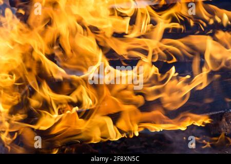 Sprurts di fiamma. Legna da ardere di legno e tronchi. La fiamma luminosa del fuoco. Materiali combustibili convertiti in carbone, fumo e cenere dal calore. Foto Stock