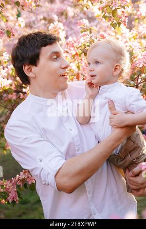 Padre con un bambino tra le braccia, sullo sfondo di un albero di mele in fiore Foto Stock