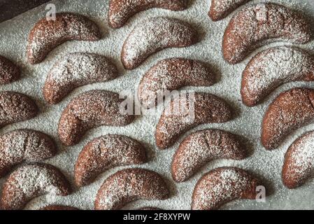 Teglia da forno con biscotti fatti in casa con nocciole a mezzaluna di cioccolato e polvere di zucchero su fondo di legno marrone. Vista dall'alto. Messa a fuoco morbida Foto Stock