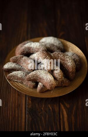 Biscotti fatti in casa nocciole crescent di cioccolato con zucchero in polvere su sfondo di legno marrone. Spazio di copia. Messa a fuoco morbida Foto Stock