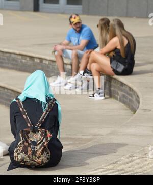 Donna musulmana in nero con hijab, di fronte a 3 persone in shorts e giubbotti Foto Stock